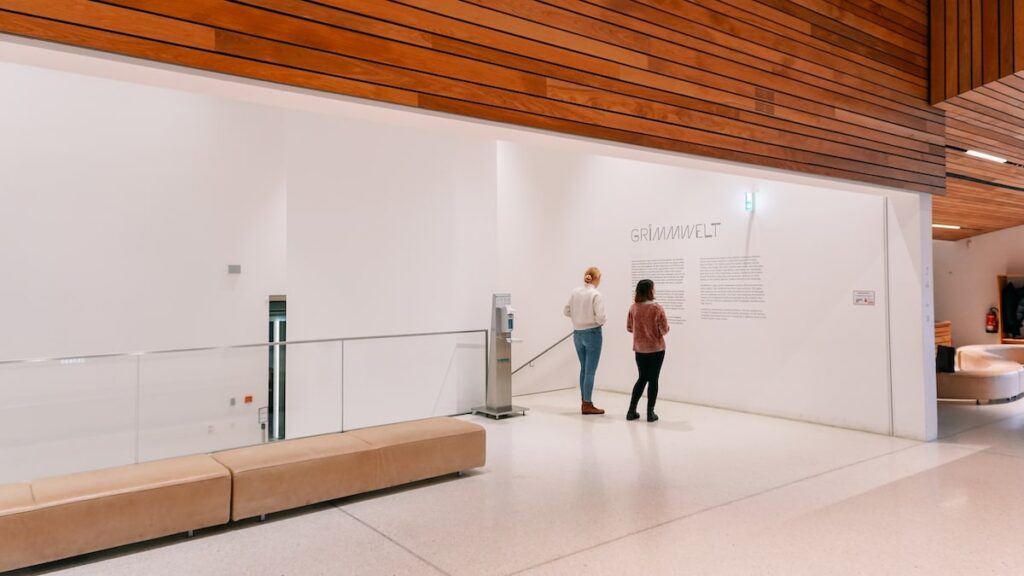 Before entering the exhibition at Grimmwelt Kassel, two women read informational material. The photo serves as a cover image for the article about Grimmwelt Kassel and the 10 facts about the Brothers Grimm accompanying it