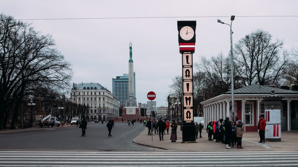 A photo depicting the iconic Laima Clock in Riga, Latvia. Behind it, you can see the Freedom Monument, one of the top things to see in Riga