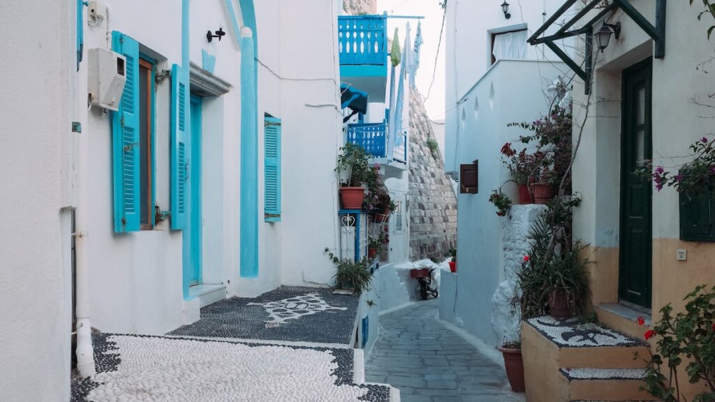 A photo of the narrow streets of Mandraki, Nisyros' main settlement, showing whitewashed houses with blue windows and traditional mosaics