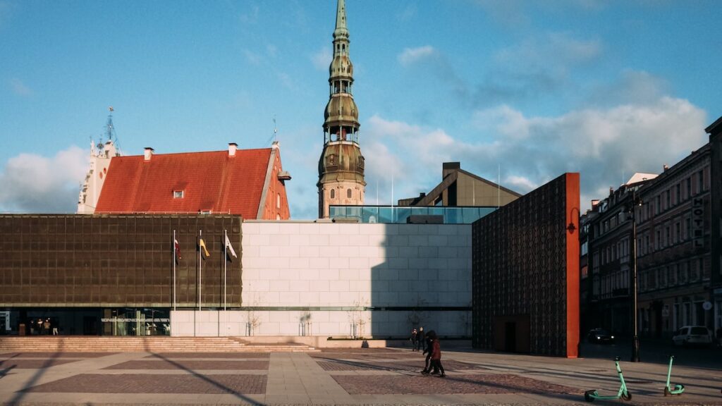 An image showing Riga landmarks on a sunny day. You can see the House of the Black Heads, the Latvia Occupation Museum, and St Peter's Cathedral from left to right.