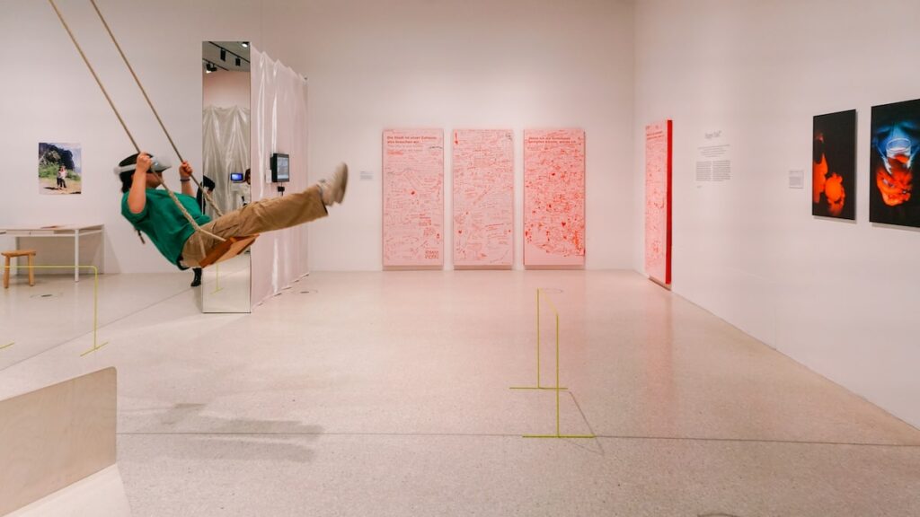 A photo from the Utopia exhibition at Grimmwelt Kassel showing paintings and a young girl wearing a Virtual Reality device