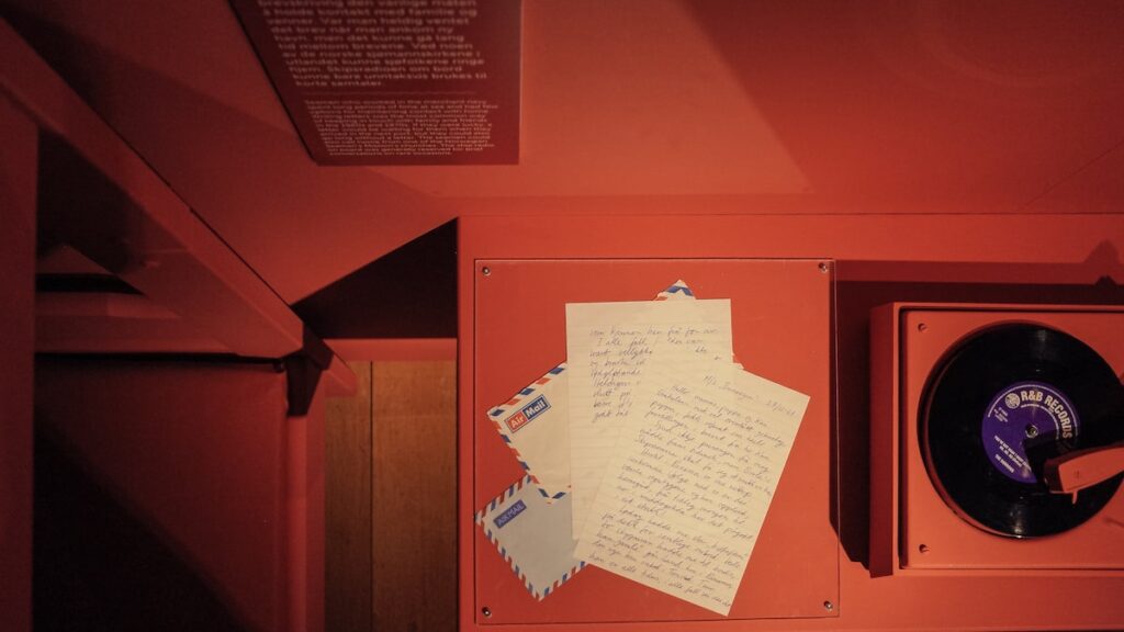 A photo from the "Queer at Sea" exhibition at the Maritime Museum of Bergen. It depicts letters written by queer sailors and vinyl, all placed on a red table