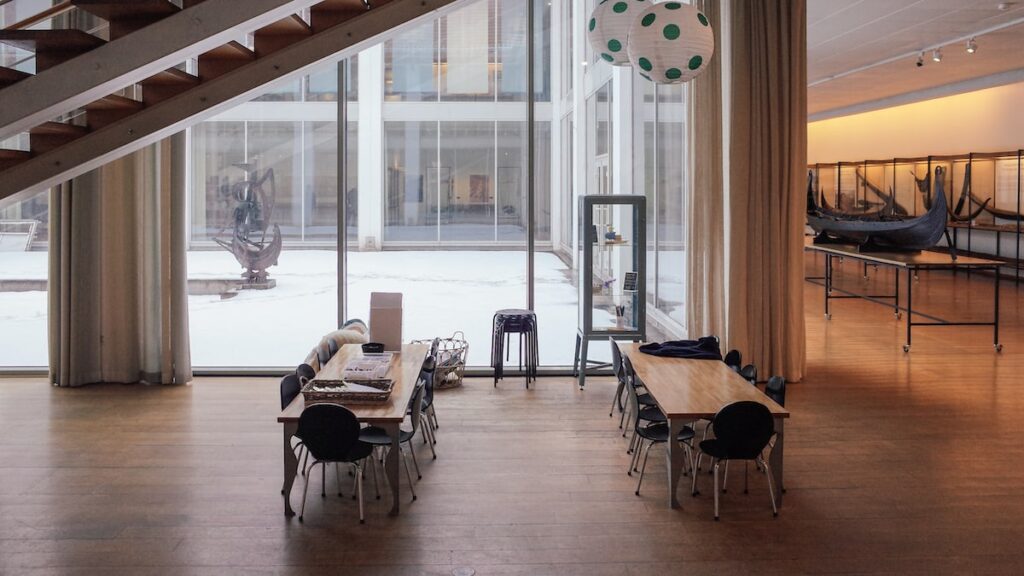A photo of the Bergen Maritime Museum interior depicts two tables with chairs and old Norwegian vessels on the right.