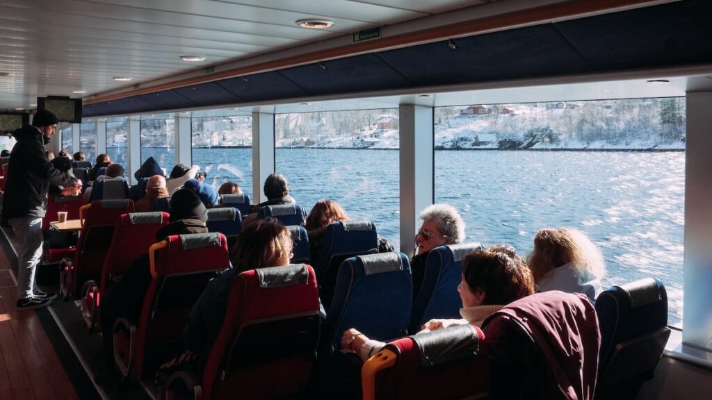 An image showing people on a sailing trip to the fjords of Norway. They are seated on the vessel's interior.