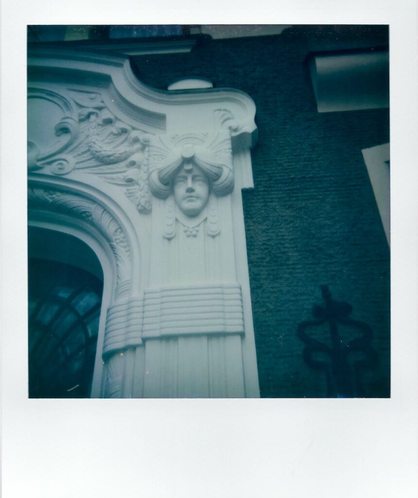 A polaroid photo of an Art Nouveau facade in Old Riga, showing a carved face on white marble.