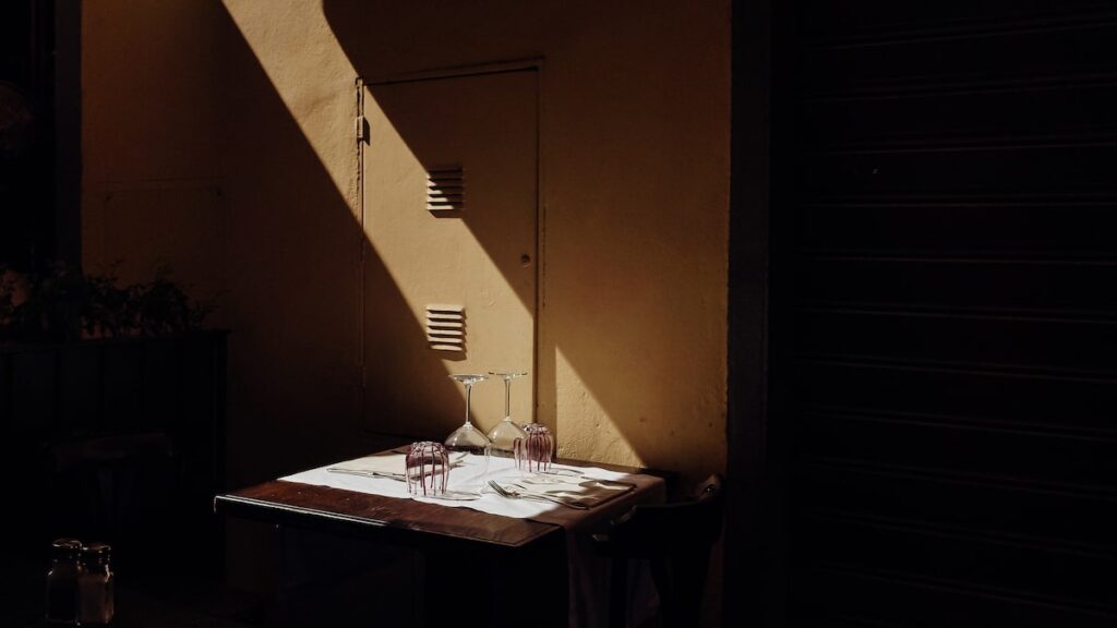 An artistic photo of a beam of light landing on wine glasses in a restaurant in Florence. The rest of the image appears somewhat dark.