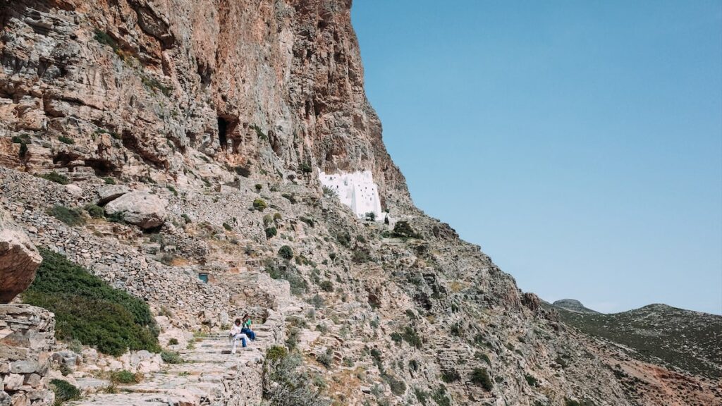 A photo showing a steep rock and the Hozoviotissa Monastery in Amorgos in the distance. It's taken shortly before starting to climb the 300 stairs to the Monastery