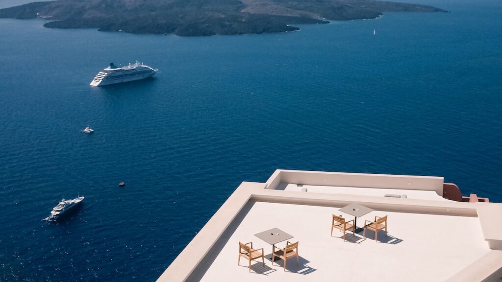 A photo of a veranda in Santorini overlooking the blue sea, with a cruise ship.