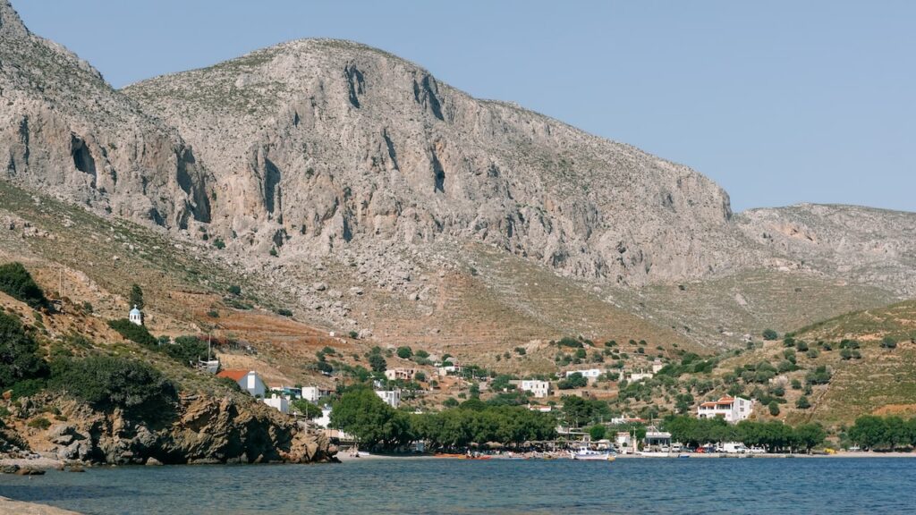 A photo of the picturesque village of Emporios in Kalymnos. The image is taken from a nearby beach and you can see the sea and impressive mountains
