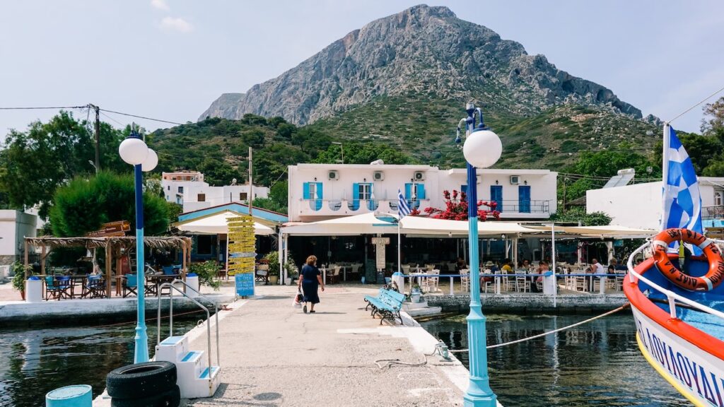 A photo showing a woman walking towards the port of Telendos in Greece