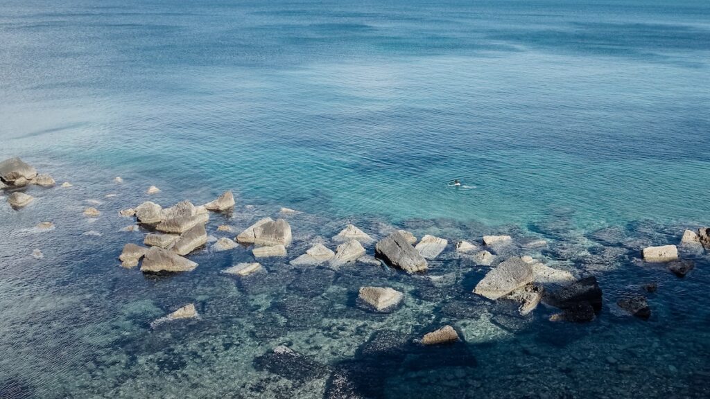 An image of a woman swimming in Syracuse, Italy, in front of rocks.