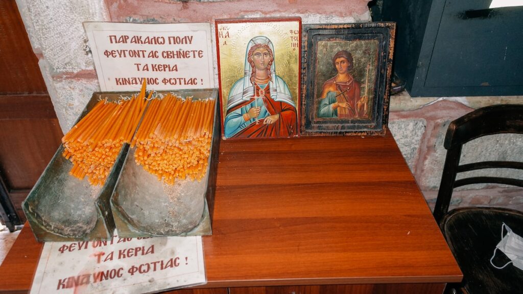 A photo of candles in Agia Fotini Church in Greece. The sign reads, "please put out the candles before leaving, danger of fire"