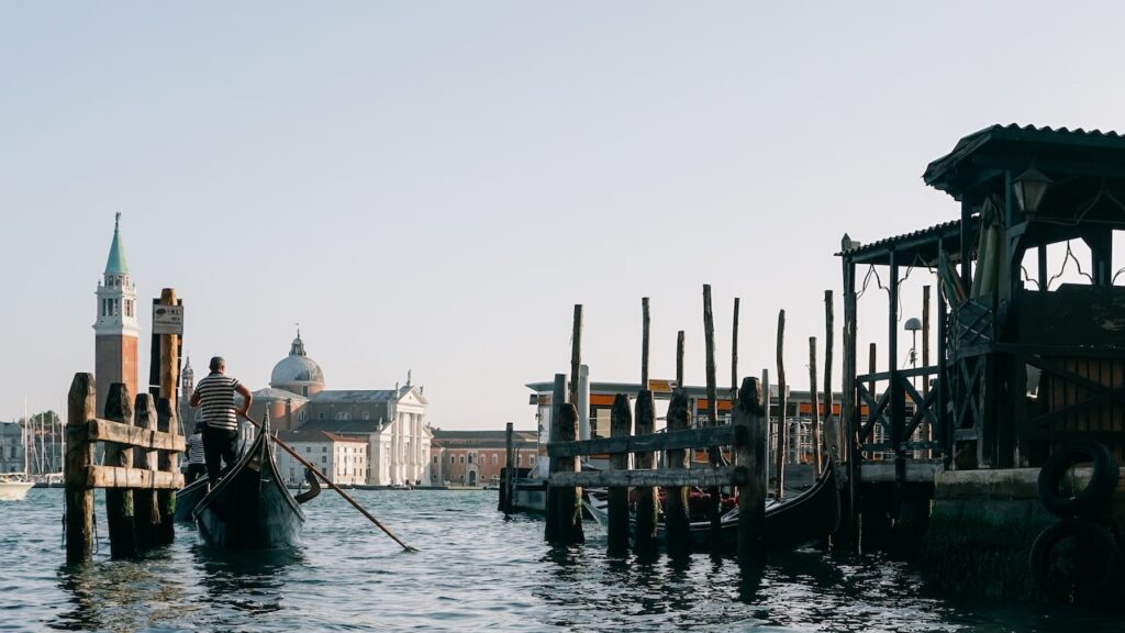 A photo showing a gondolier with the island of San Giorgio Maggiore in the background. This POV photo is taken during a gondola ride in Venice, Italy.