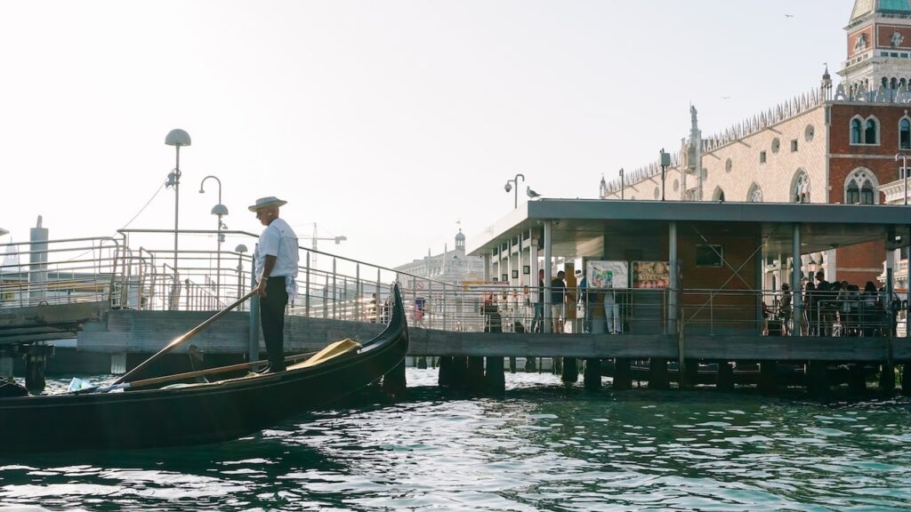 A photo showing a gondolier during a gondola ride in Venice. Behind him you can see the Doge's Palace in Saint Mark's Square