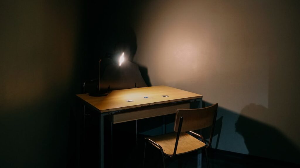 A photo of an interrogation room at the DDR Museum Berlin, portraying a two chairs, a desk and a lamp