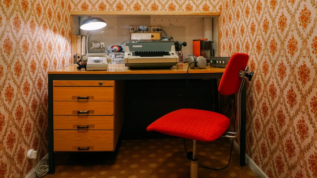 A photo of a small room containing a red chair and a typewriter used for surveillance reports in the former East Berlin
