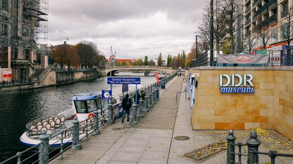 A photo of the DDR Museum Berlin exterior, with a cruise boat on the left and glimpses of the Berliner Dom