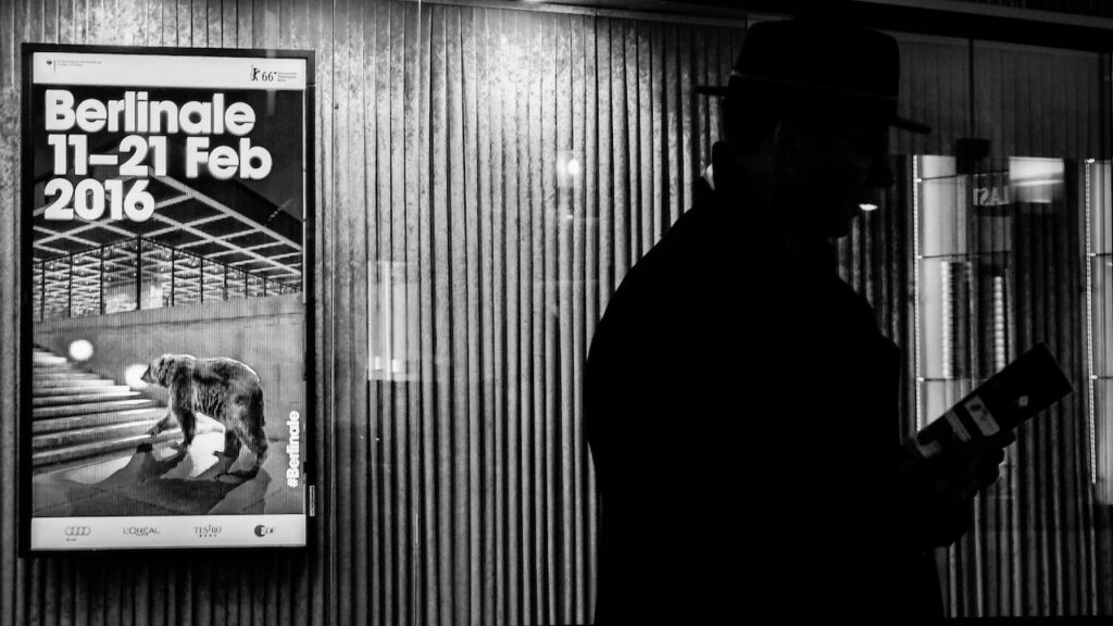 A photo of the poster of Berlinale 2016 at Zoo Palast and a man reading the festival's program