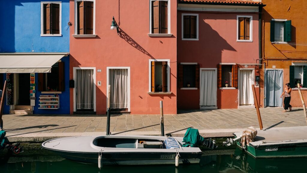 A photos portraying various colorful houses in Burano, Italy, with some motorboats parked in the canal