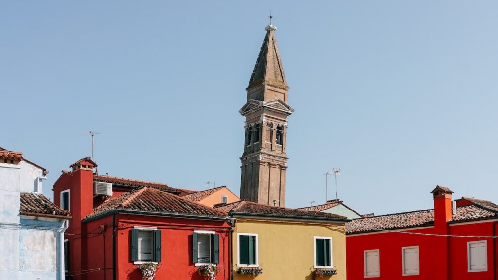 A photo showing colorful houses and in the background the Leaning Tower of Burano island in Venice