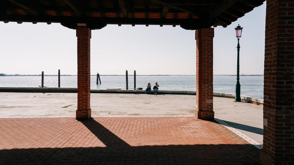 A photo showing two women sitting next to the Venice lagoon in Burano, Italy
