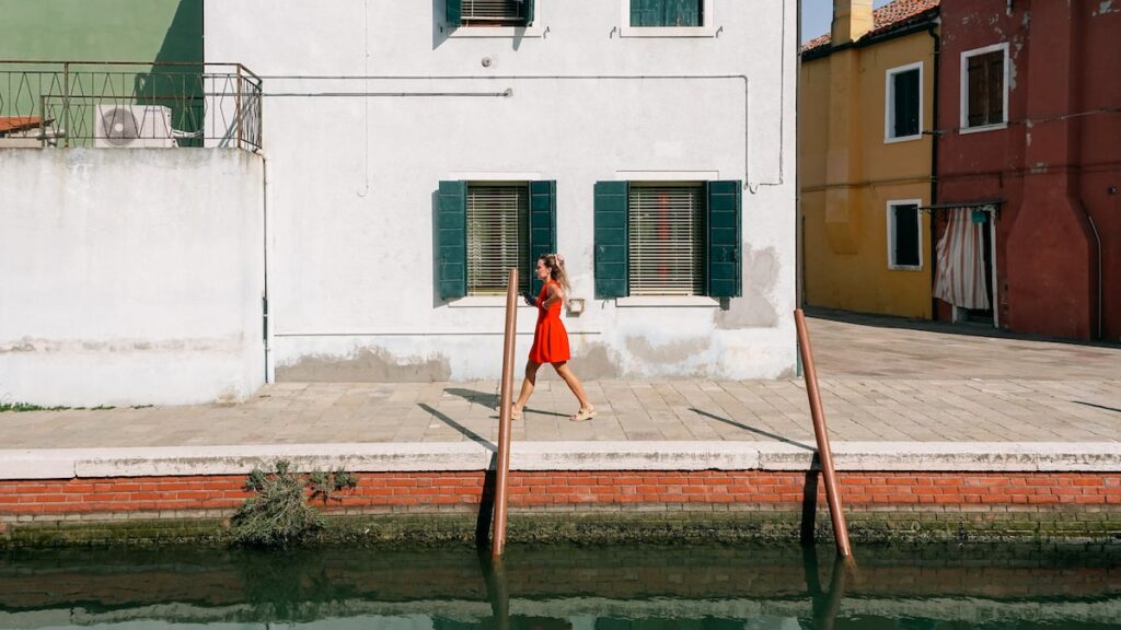 A photo showing a woman in red walking in the streets of Burano, Italy