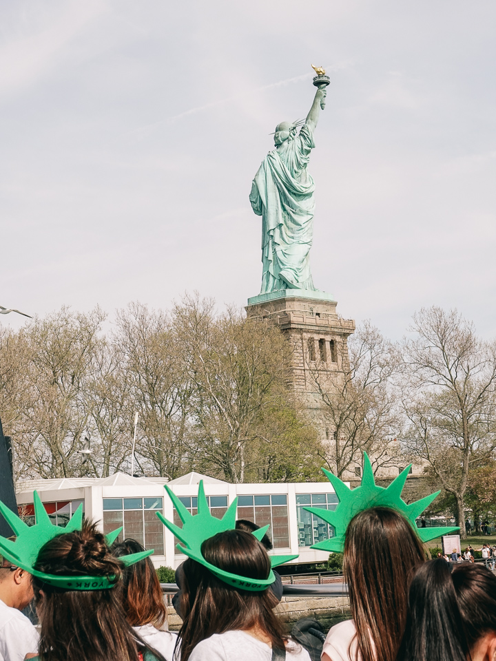 Travelers wearing green crowns and the Statue of Liberty in the background