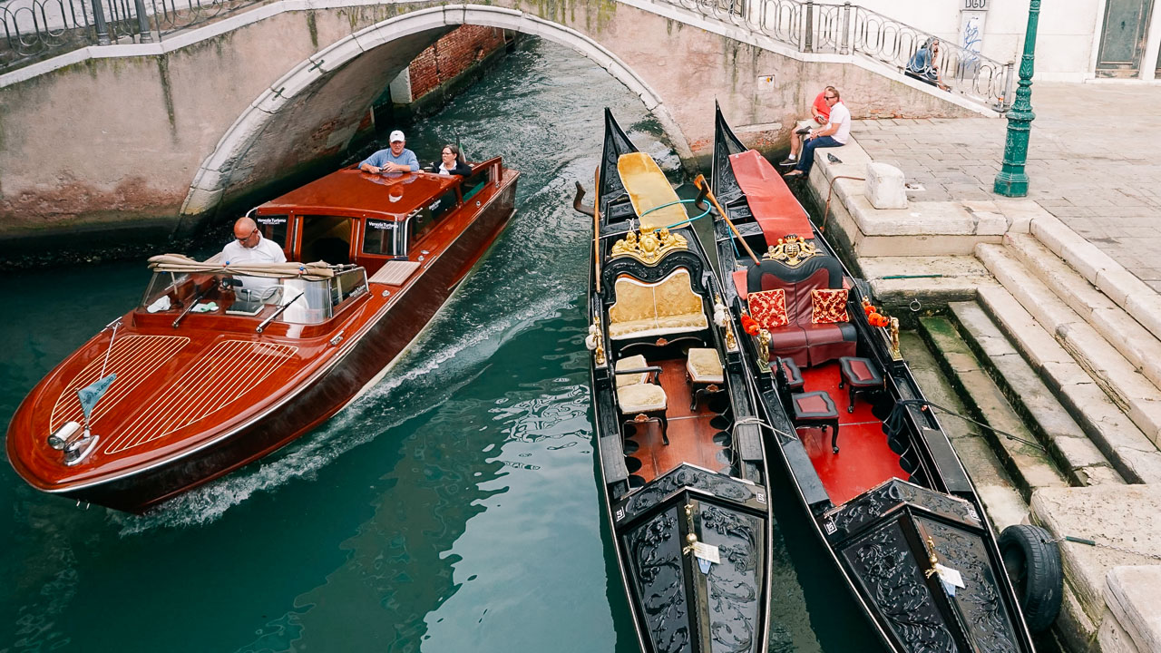 A water taxi driving next to two parked gondolas in Venice