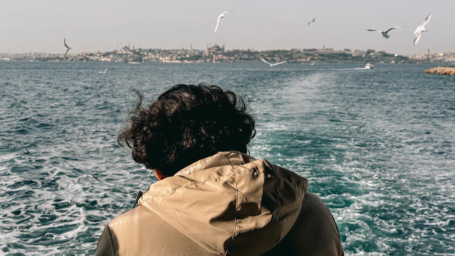 A man enjoying the crossing of Bosporus on a Karaköy to Kadıköy ferry with seagulls flying around him